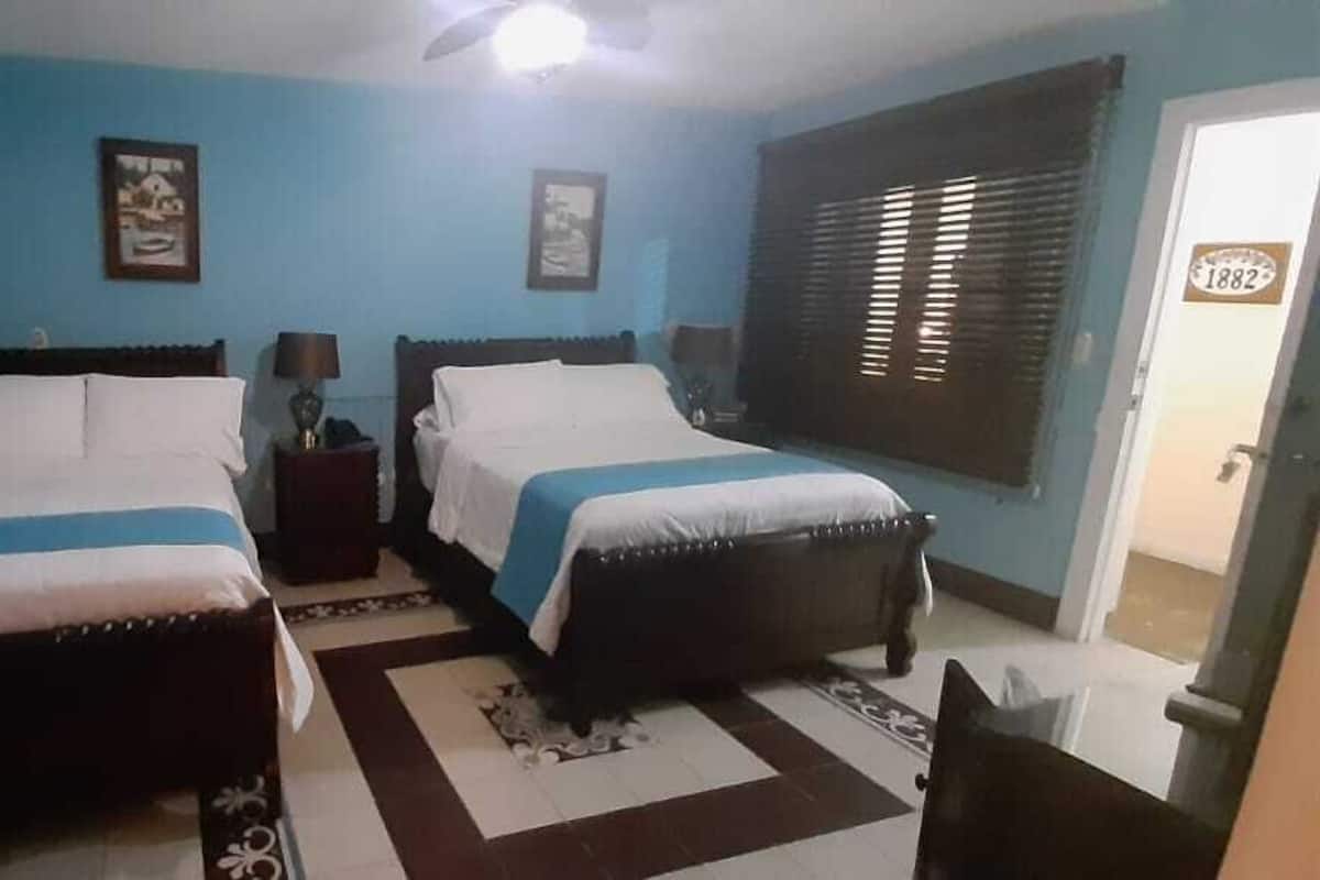 Une chambre avec deux lits, une table de chevet, une lampe et une fenêtre avec des stores.