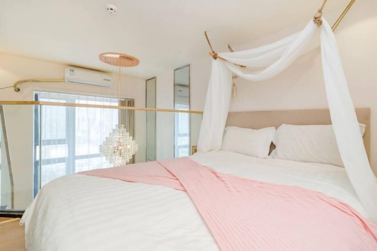 A bedroom with a canopy bed, a large window, and a chandelier.
