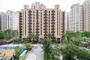 Un edificio residencial alto con varios balcones, rodeado de vegetación y un parque infantil.