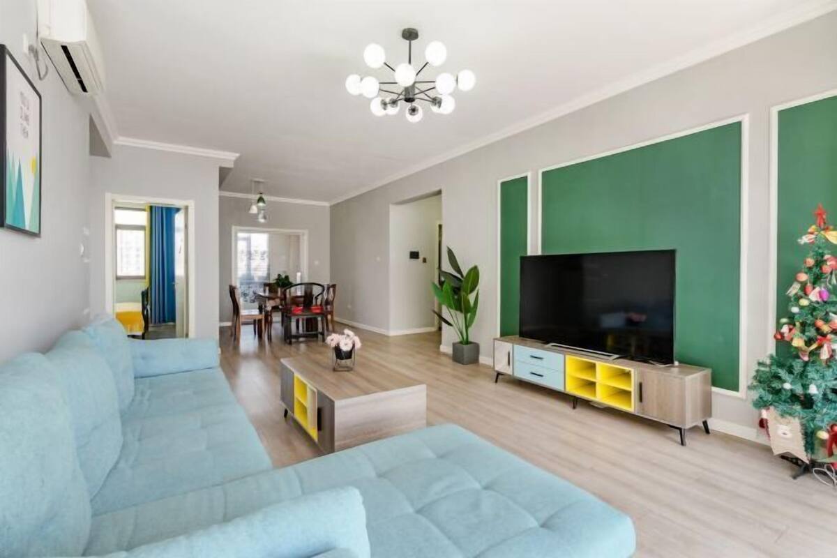 A modern living room with a light blue sofa, a flat-screen TV, and a green accent wall.