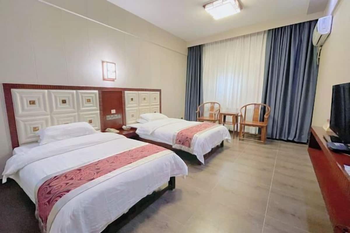 A hotel room with two beds, a desk, a chair, and a television.