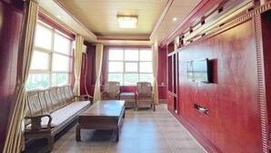 A room with a sofa, a table, and chairs, a television, and large windows. - Hongli Business Hotel (Tunchang)