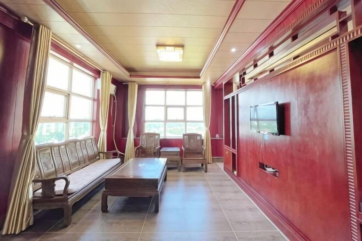 A room with a sofa, a table, and chairs, a television, and large windows.