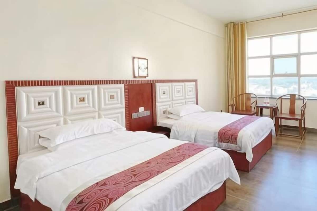 A hotel room with two beds, a window with curtains, a chair, and a small table.