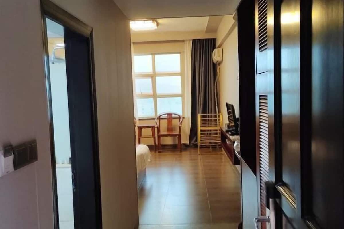 A hotel corridor with a wooden floor, a chair, a desk, and a window with curtains.