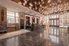 Um hall amplo com piso de mármore polido, balcão de recepção e uma grande janela que oferece luz natural.