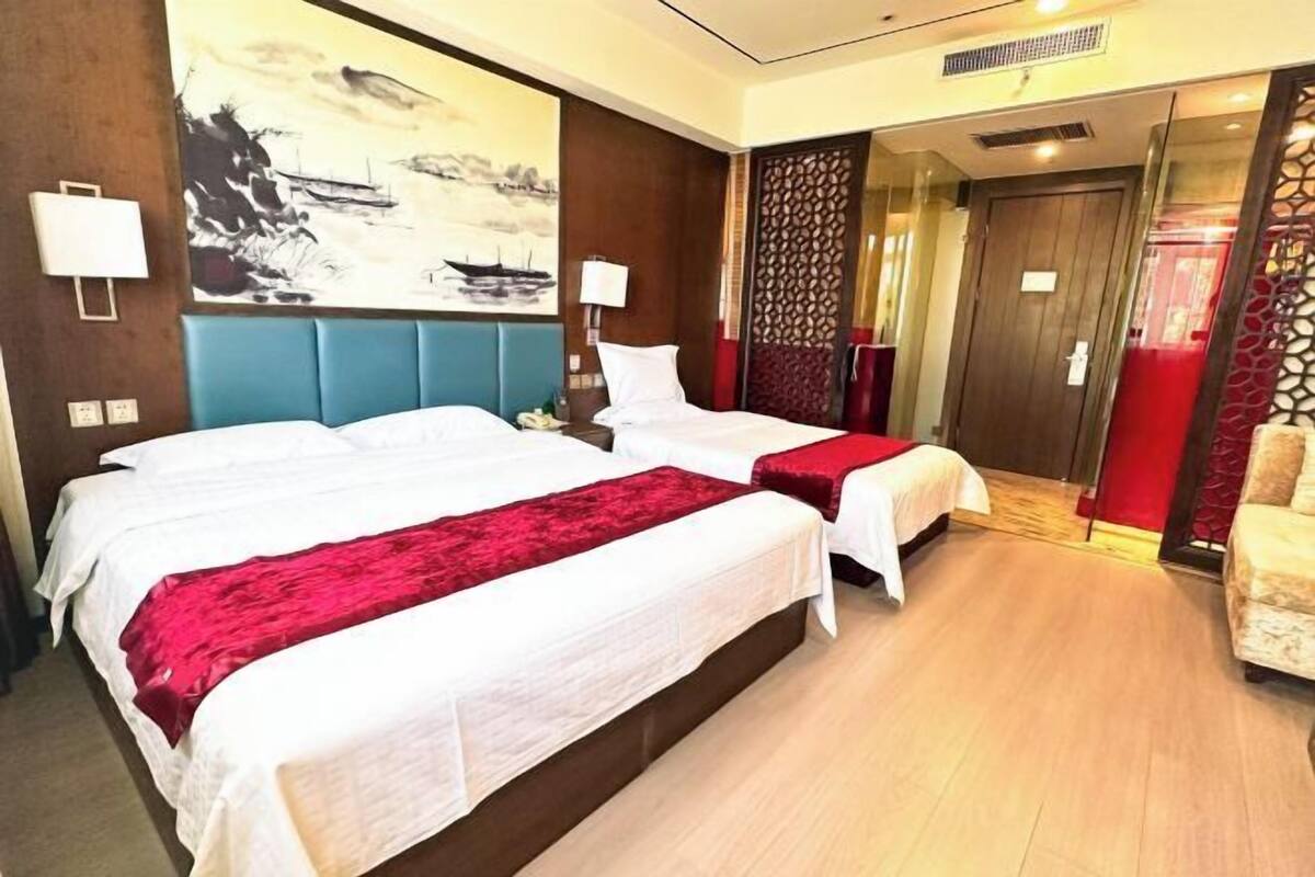 Una habitación de hotel con dos camas, un cuadro grande en la pared y un separador decorativo rojo.
