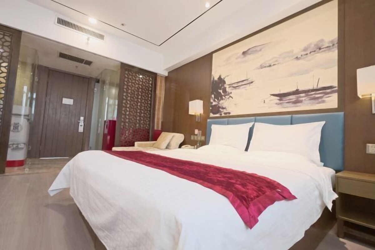 A modern hotel room with a large bed, a seating area, and a painting on the wall.