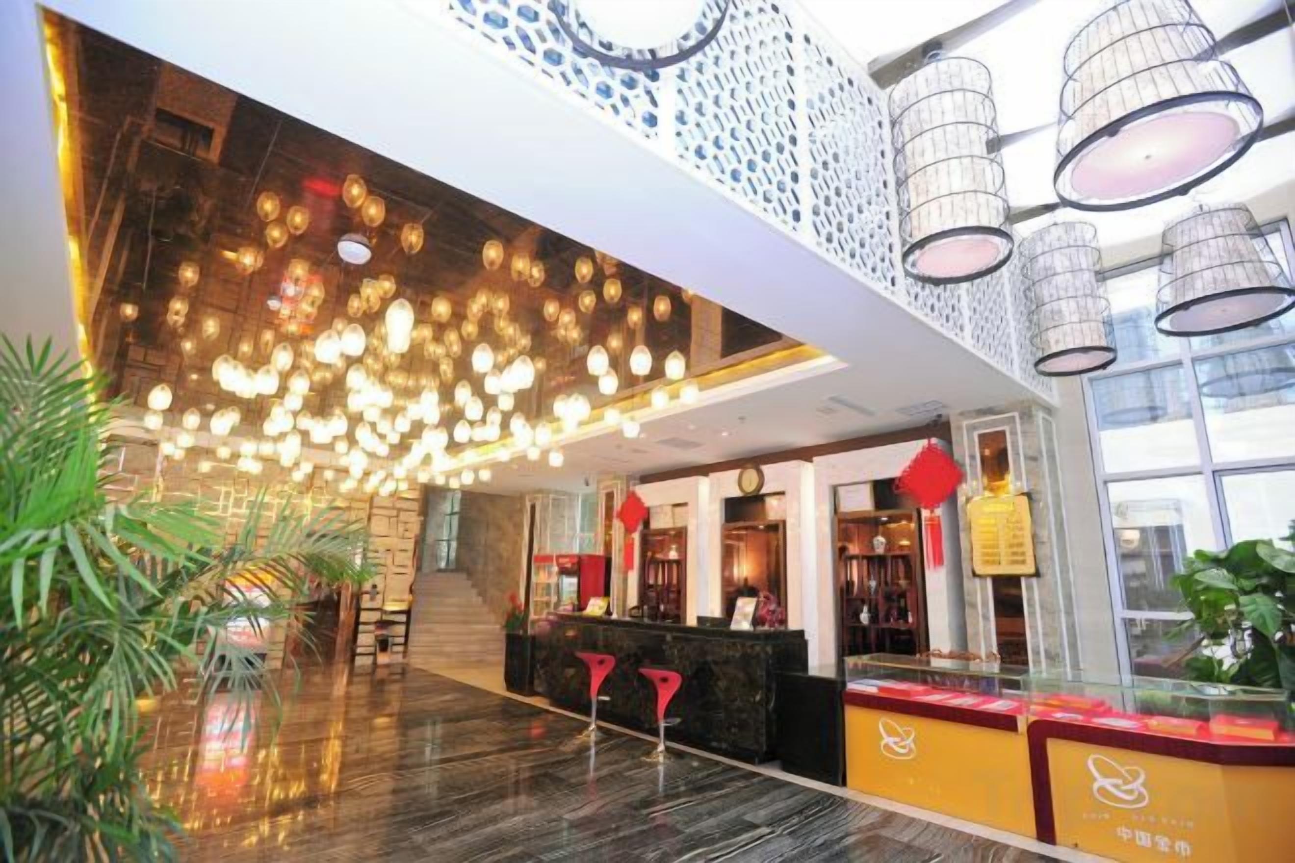 A hotel lobby with a reception desk, a staircase, and a ceiling with hanging lights.