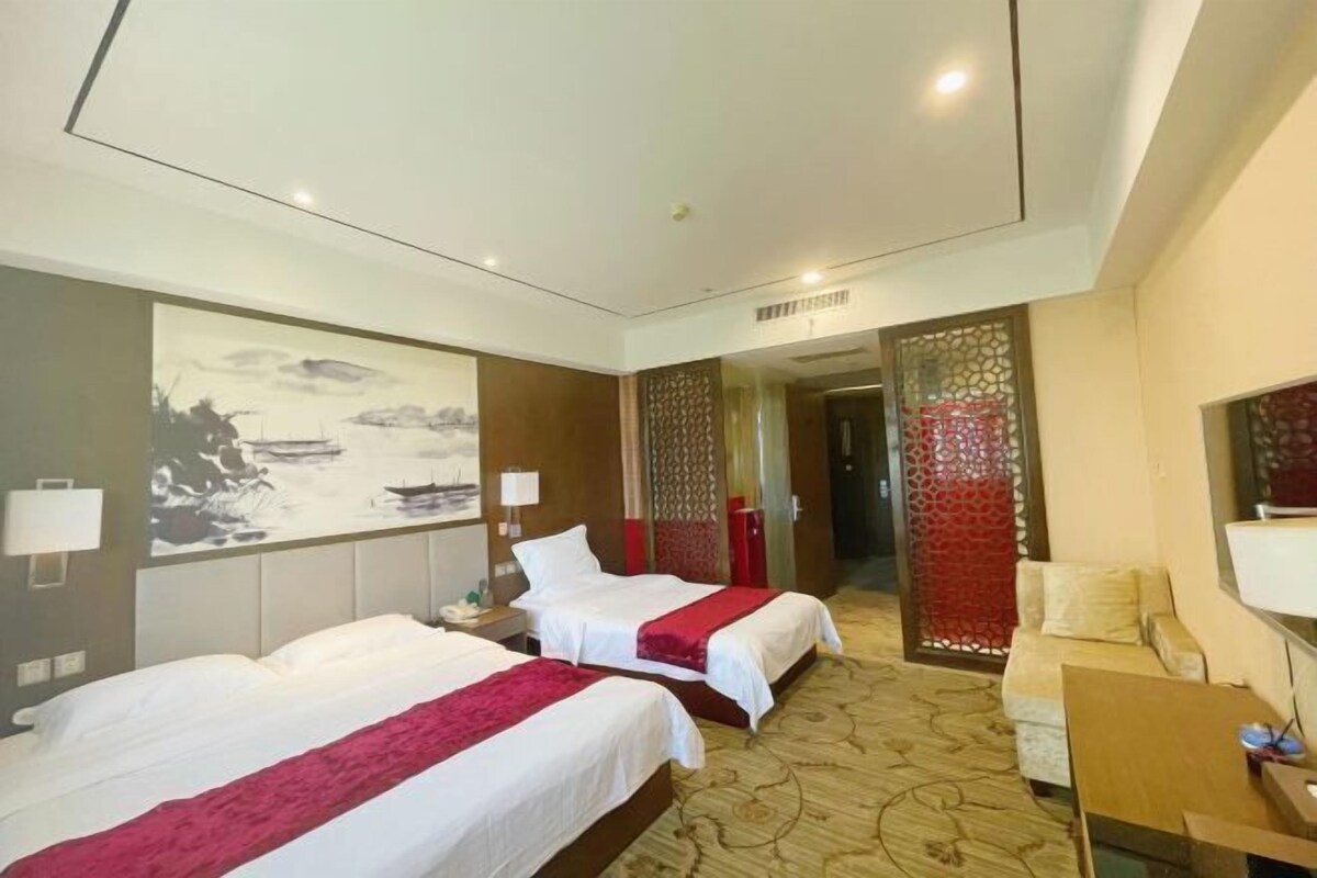 A hotel room with two beds, a sofa, a desk, and a decorative wall.