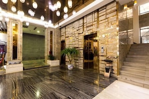 Vestíbulo de hotel con piso de mármol, un mostrador de recepción, una escalera y una pared con diseño geométrico.