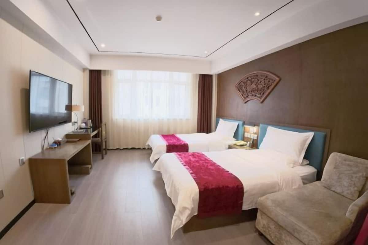 Una habitación de hotel con dos camas, televisión, escritorio y sofá.