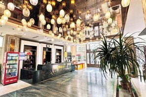 Een ruime lobby met een receptiebalie, een automaat en een grote kamerplant.