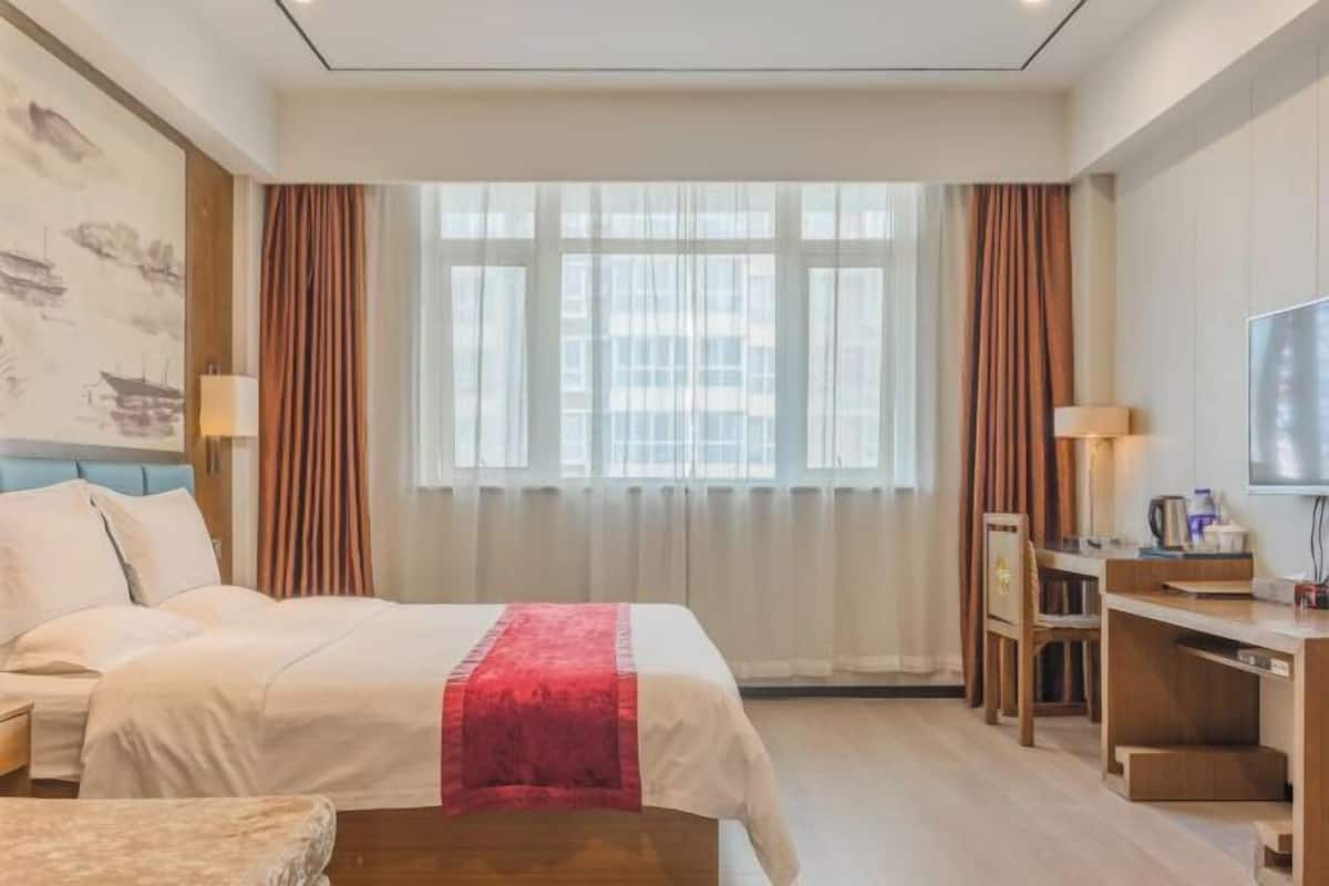 Habitación de hotel con cama, escritorio, silla, televisor y ventana con cortinas.