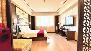 Quarto de hotel com cama, escrivaninha, televisão e janela com cortinas.