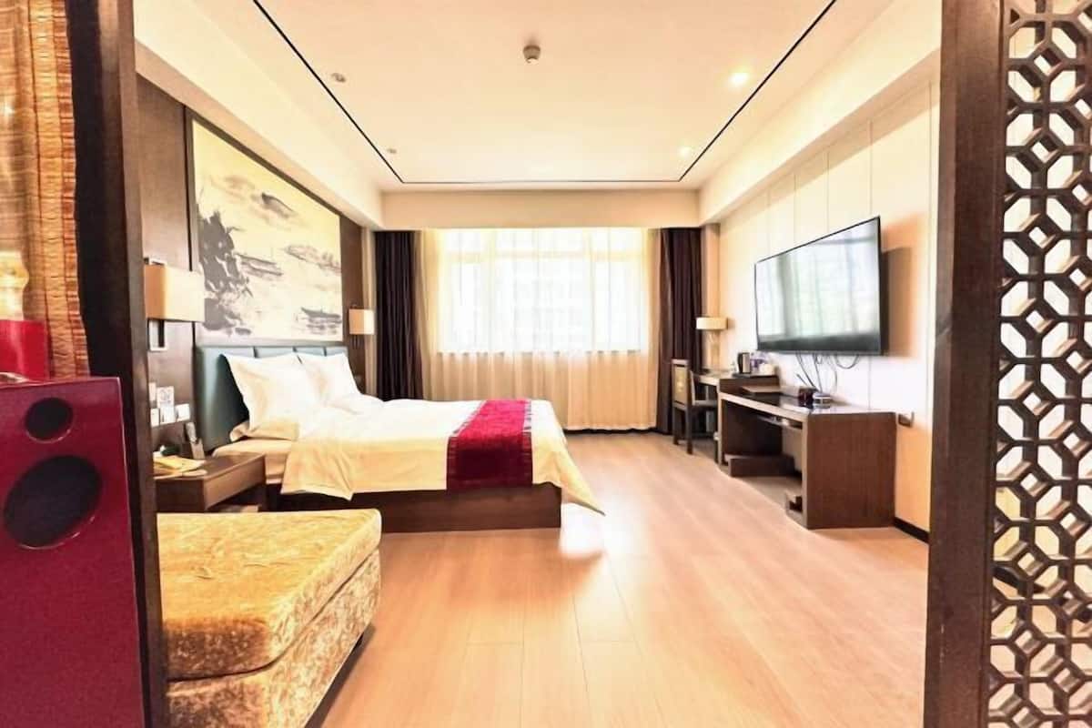 Una habitación de hotel con cama, escritorio, televisor y ventana con cortinas.