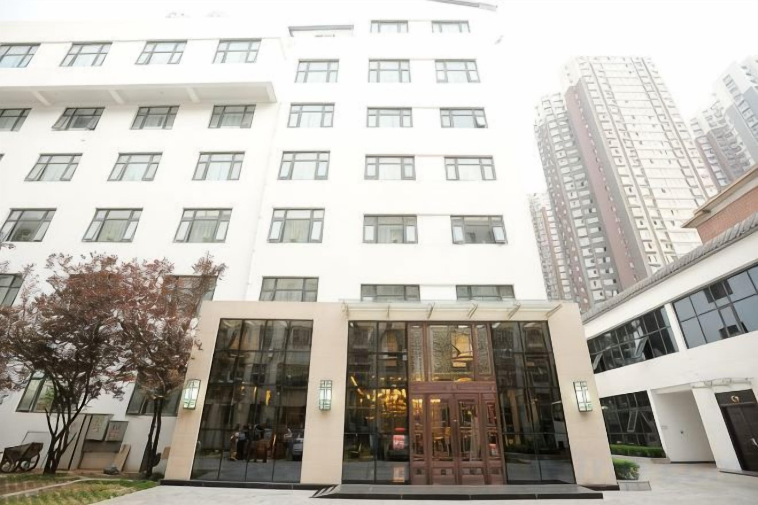 A hotel entrance with a glass facade, a central door, and a small garden area.