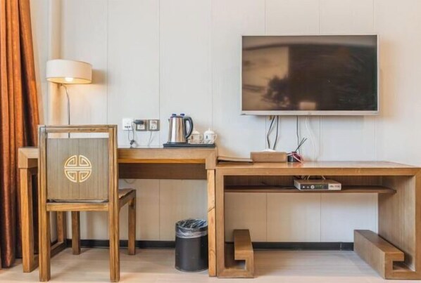 A compact hotel room with a wooden desk, a television mounted on the wall, a lamp, and a trash bin. - Wujia Yizhan Boutique Inn (Zhengzhou)