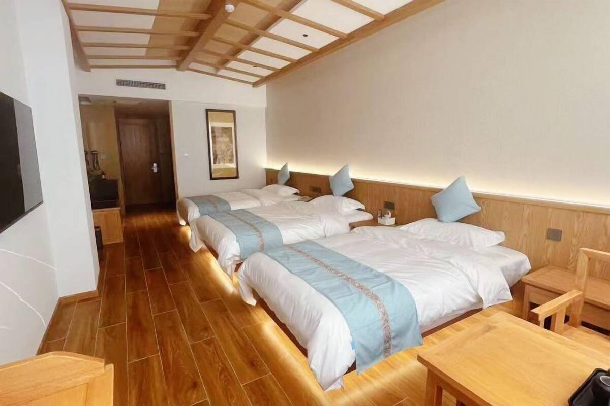 Ett hotellrum med två sängar, trägolv, ett träpanelat tak, ett litet bord och en stol.