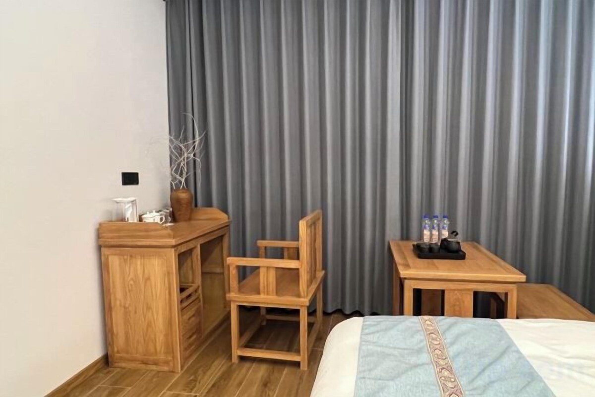 Habitación de hotel con cama, escritorio, silla, una mesita con botellas y cortina.