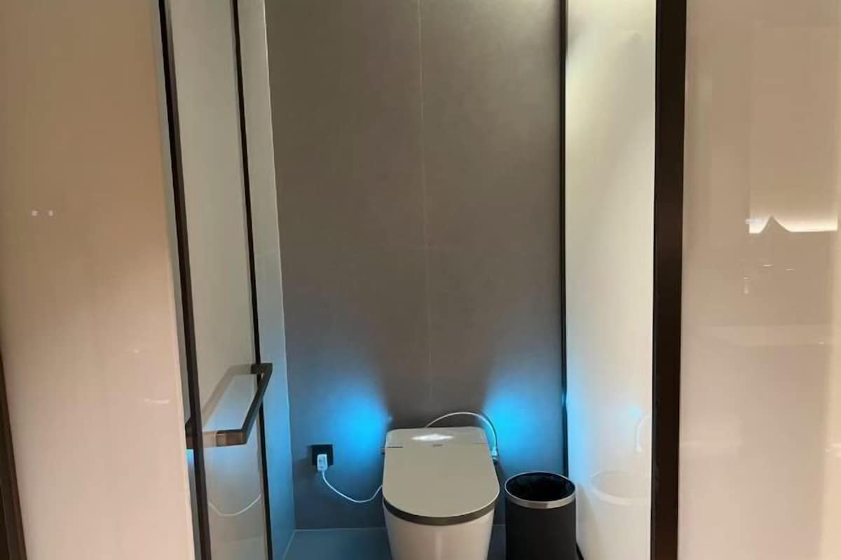 A modern bathroom with a toilet, a trash bin, and a wall-mounted outlet.