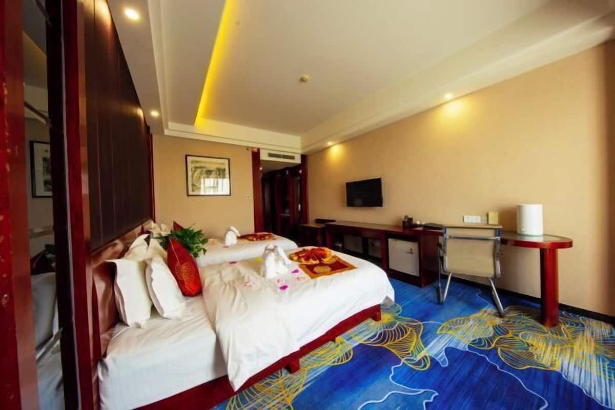 Habitación de hotel con una cama grande, un escritorio, un televisor y una alfombra con diseño azul y amarillo.