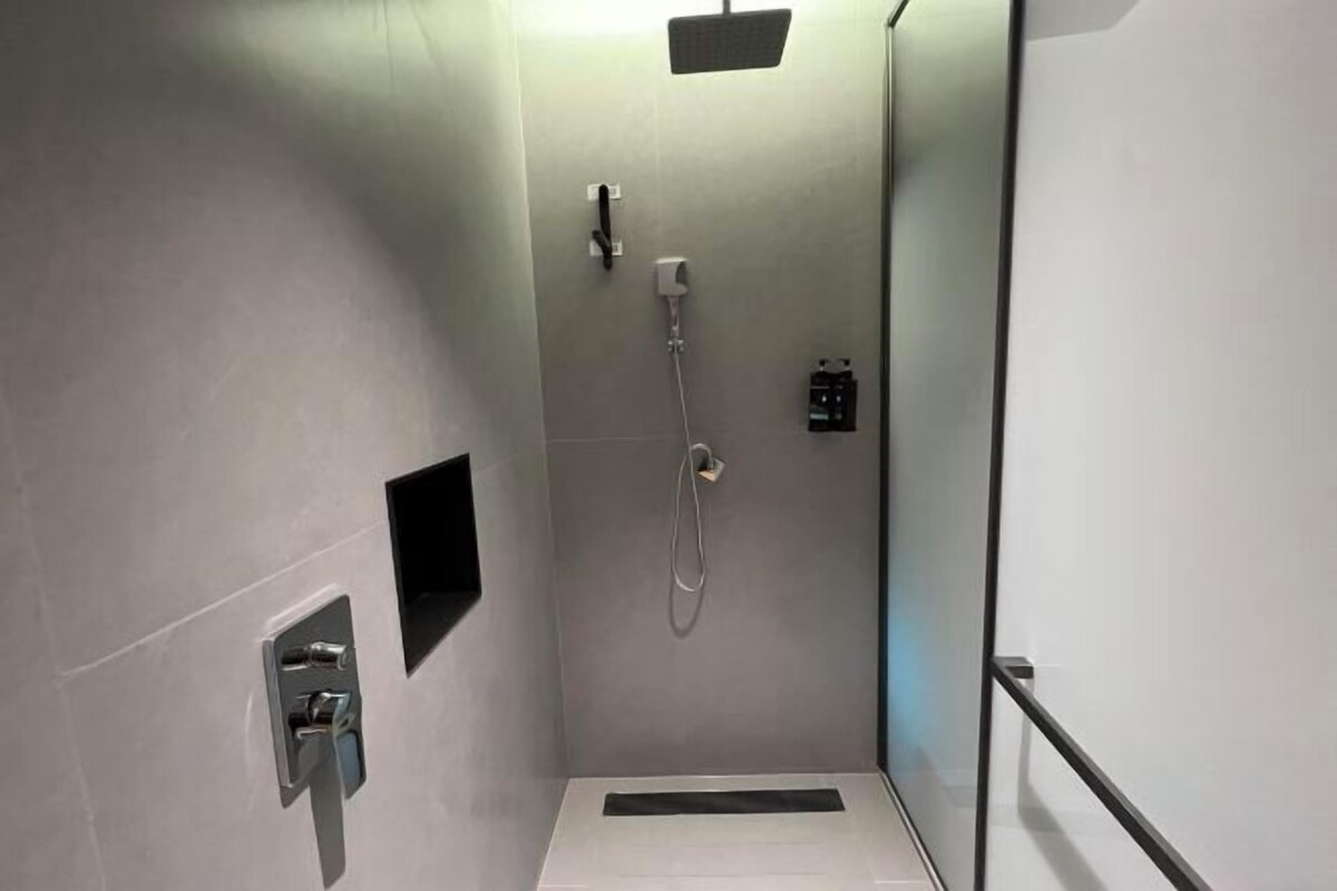 A modern shower area with a glass door, a handheld showerhead, and a wall-mounted control panel.