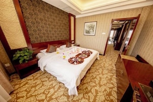 Habitación de hotel con una cama grande, una mesita de noche, un aparador y una planta.