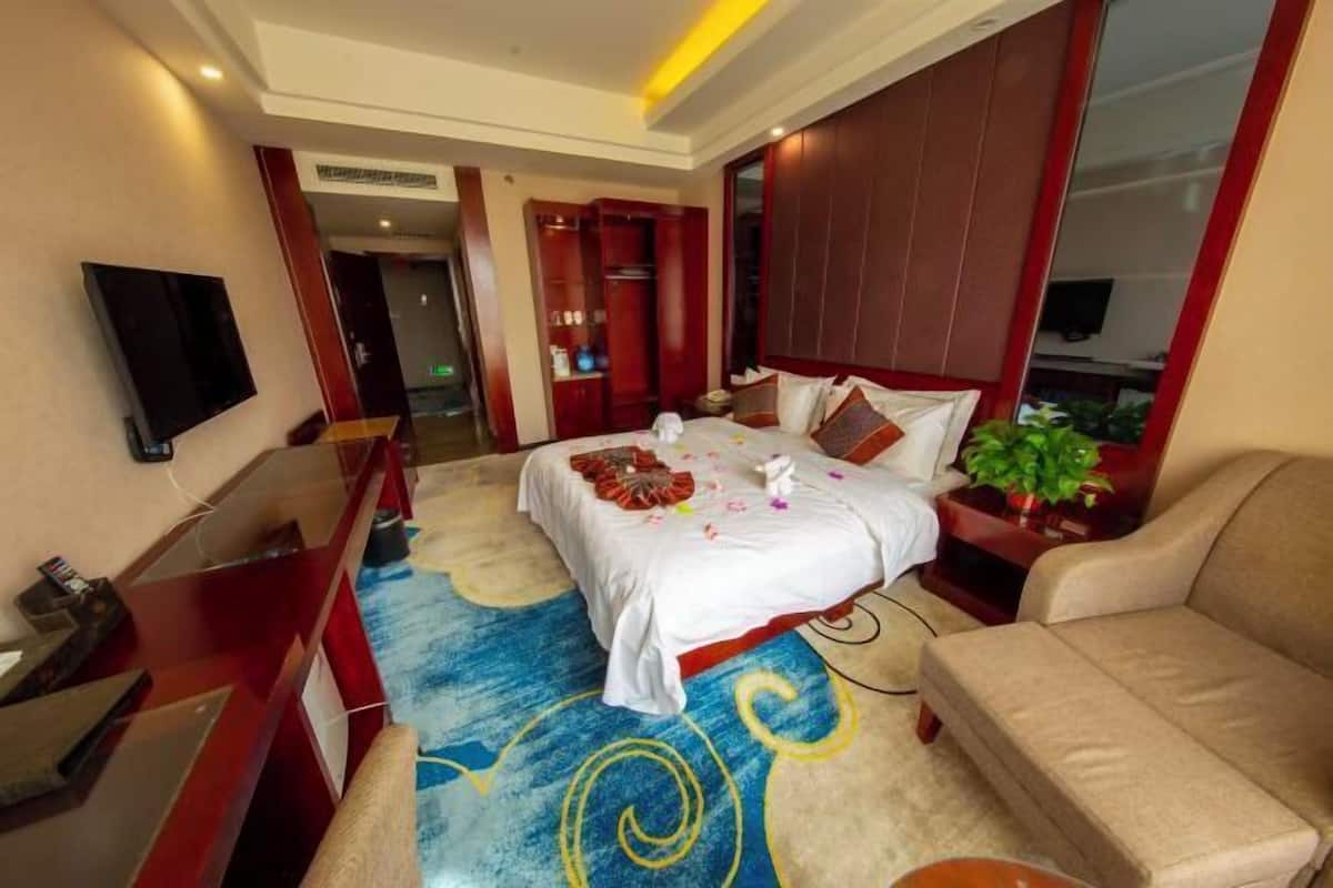 Una habitación de hotel con cama, escritorio, televisión, sofá y planta.