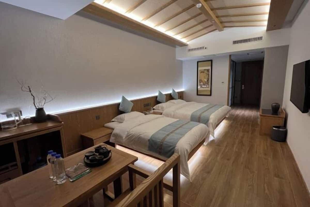 Habitación de hotel con dos camas, un escritorio de madera con una silla, una mesita y un televisor montado en la pared.