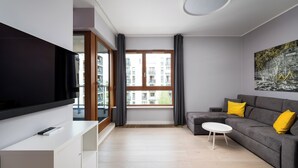 Una sala de estar moderna con un sofá gris, una mesa de centro blanca y un televisor de pantalla plana sobre un mueble blanco.