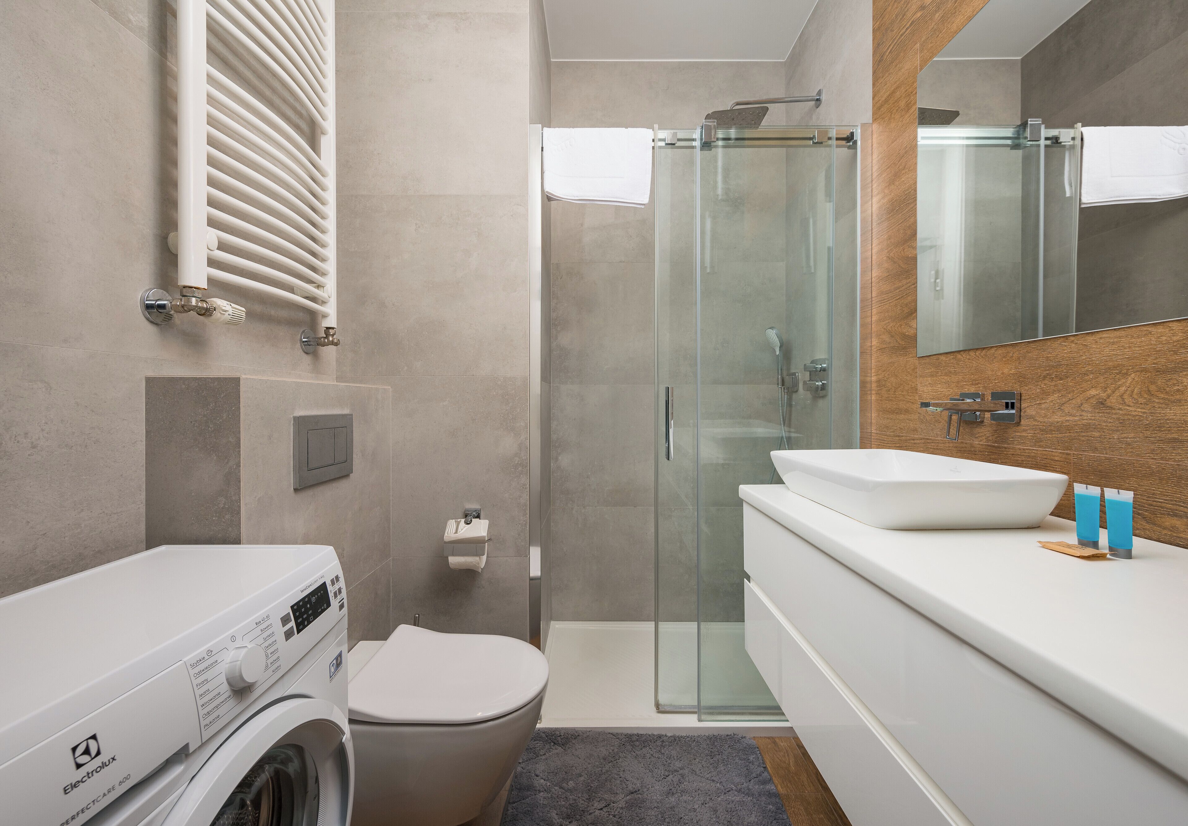 Une salle de bain moderne avec une douche à parois de verre, des toilettes blanches, un lave-linge et un lavabo doté d'un plan de travail en bois.