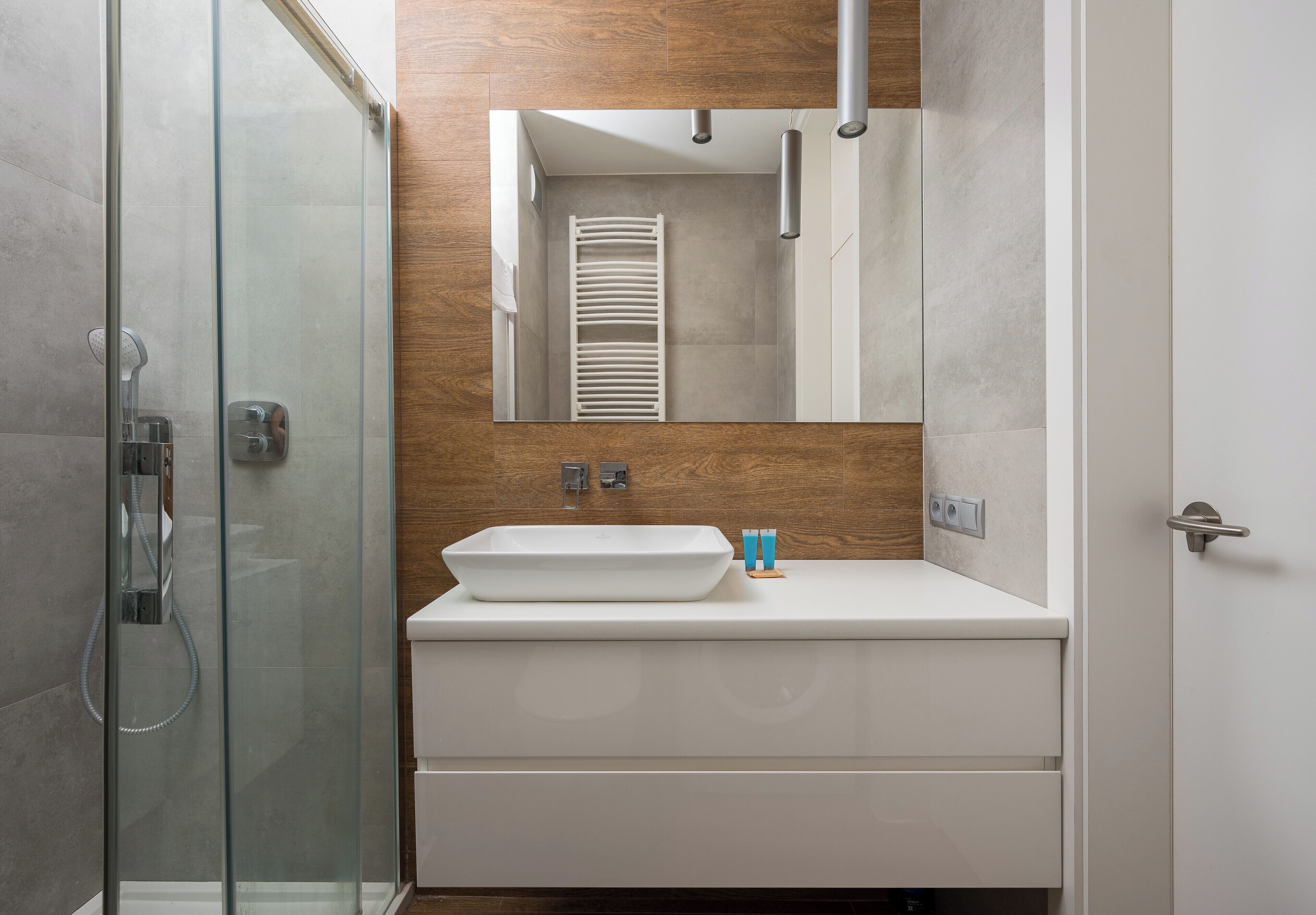 Un baño moderno con cabina de ducha de vidrio, un lavabo blanco y un mueble de tocador de madera.