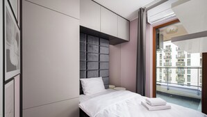 Un dormitorio moderno con cama, almacenamiento integrado, ventana con vistas a edificios y un equipo de aire acondicionado instalado en el techo.