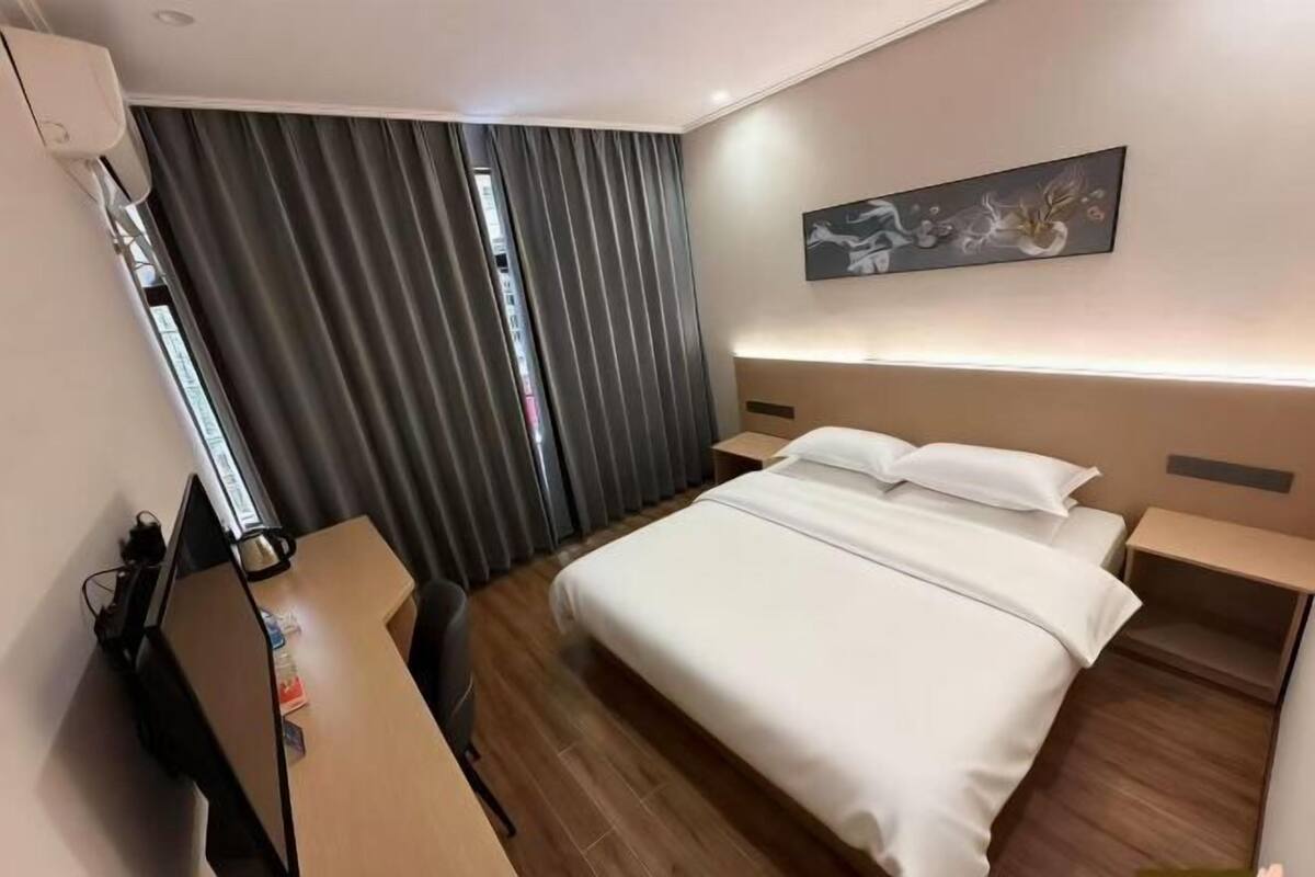 Hotellihuone, jossa on sänky, työpöytä, tuoli, seinälle ripustettu taideteos ja ikkuna, jossa on verhot.