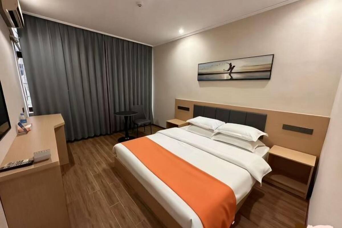 Hotellihuone, jossa on sänky, työpöytä, tuoli, pieni pöytä, seinällä taulu ja ikkuna, jossa on verhot.