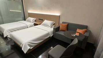 A hotel room with two beds, a sofa, a small table, and a chair.