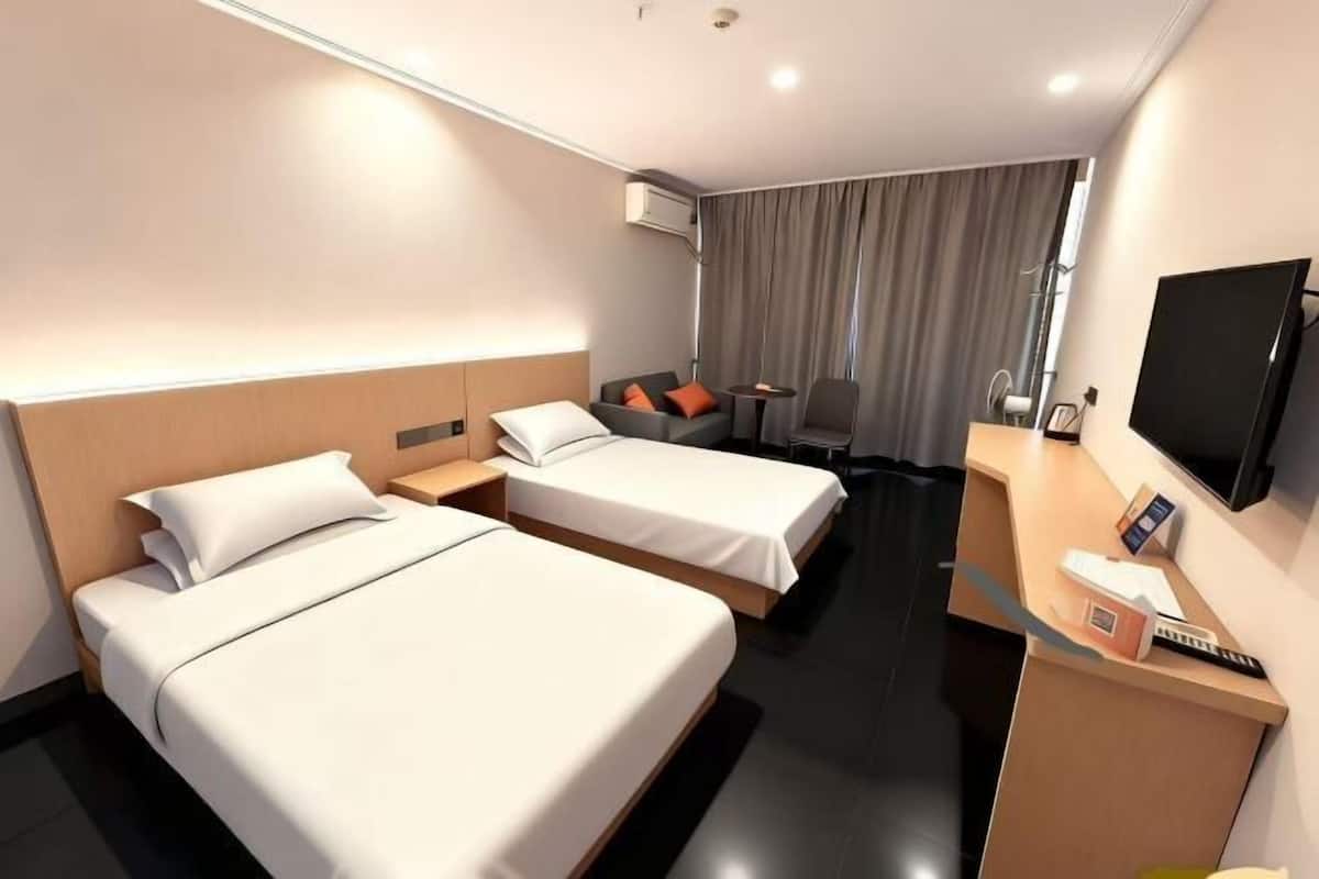 Hotellihuone, jossa on kaksi sänkyä, työpöytä, televisio ja ikkuna, jossa on verhot.