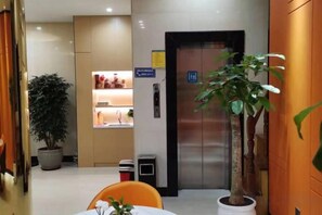 A hotel lobby with a reception desk, a potted plant, an elevator, and a trash bin. - Wenzhou Jinyuan Hotel (Wenzhou)