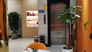 Eine Hotellobby mit einer Rezeption, einer Zimmerpflanze, einem Aufzug und einem Mülleimer.