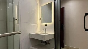 Ein modernes Badezimmer mit Duschkabine aus Glas, Marmorwaschbecken und einem wandmontierten Spiegel.