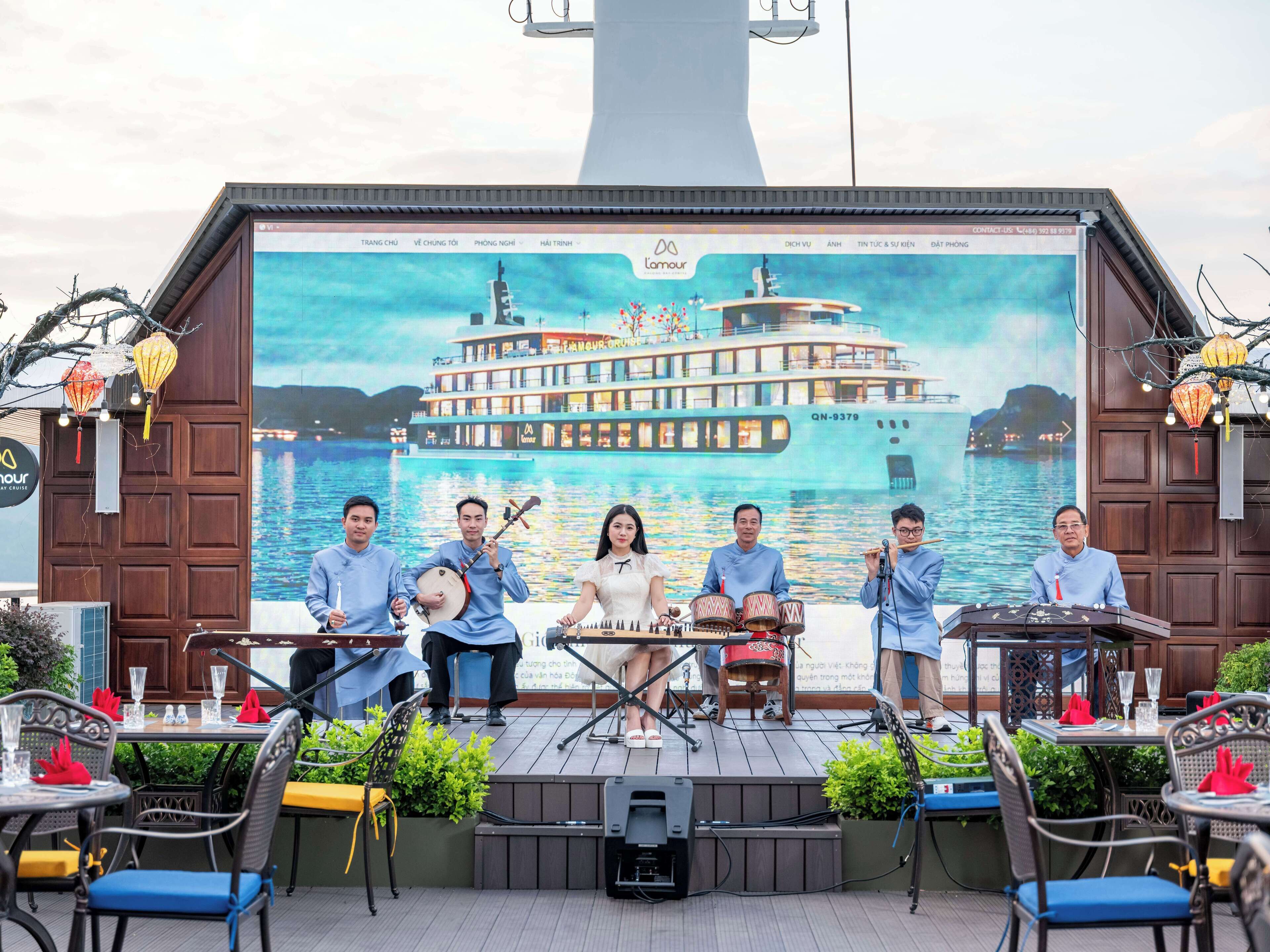 Une scène où un groupe de personnes se produit, un grand écran sur lequel est affiché un bateau, et des espaces de repos en plein air avec des tables et des chaises.