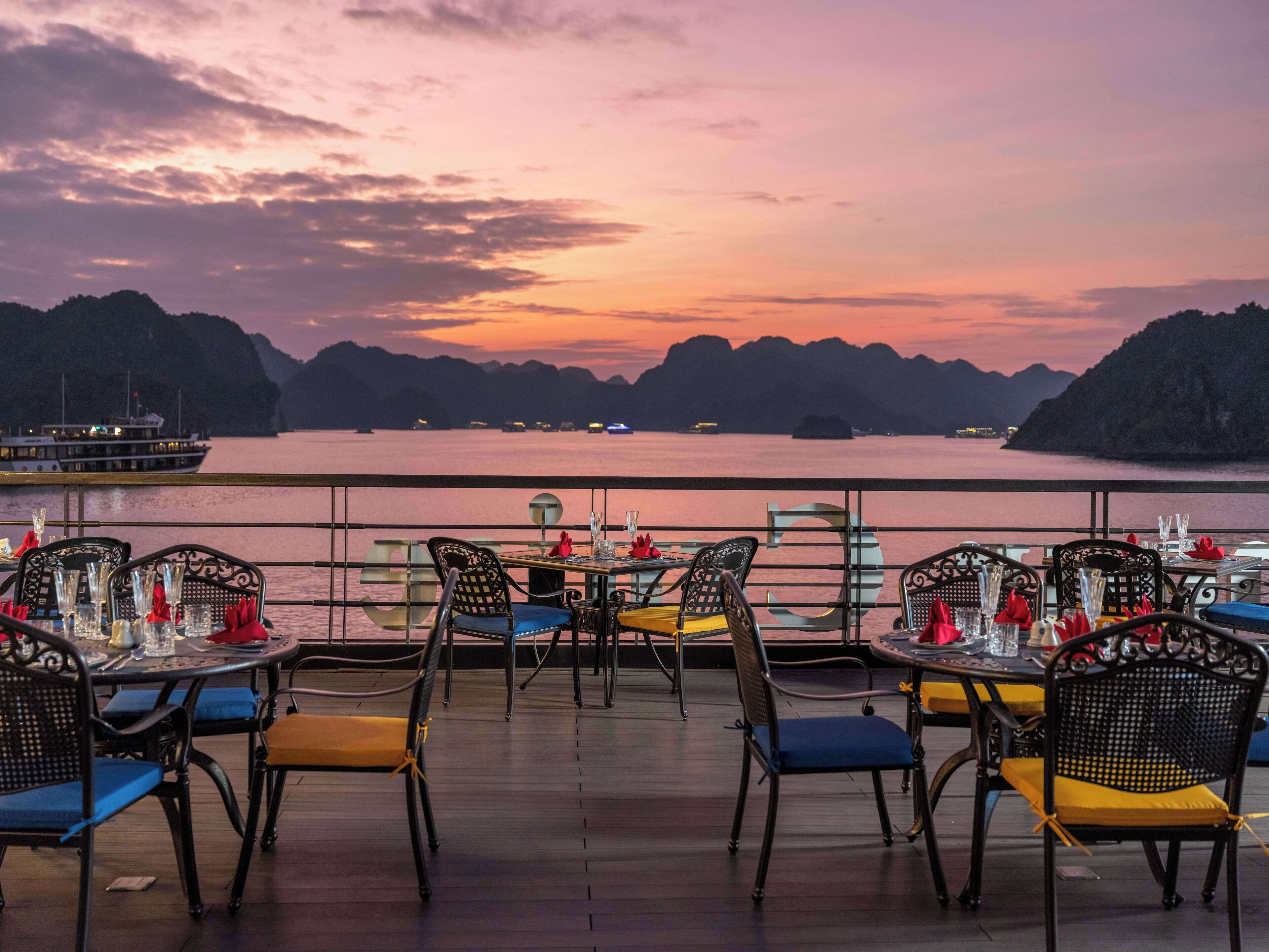 A restaurant with tables and chairs facing a body of water and distant hills.