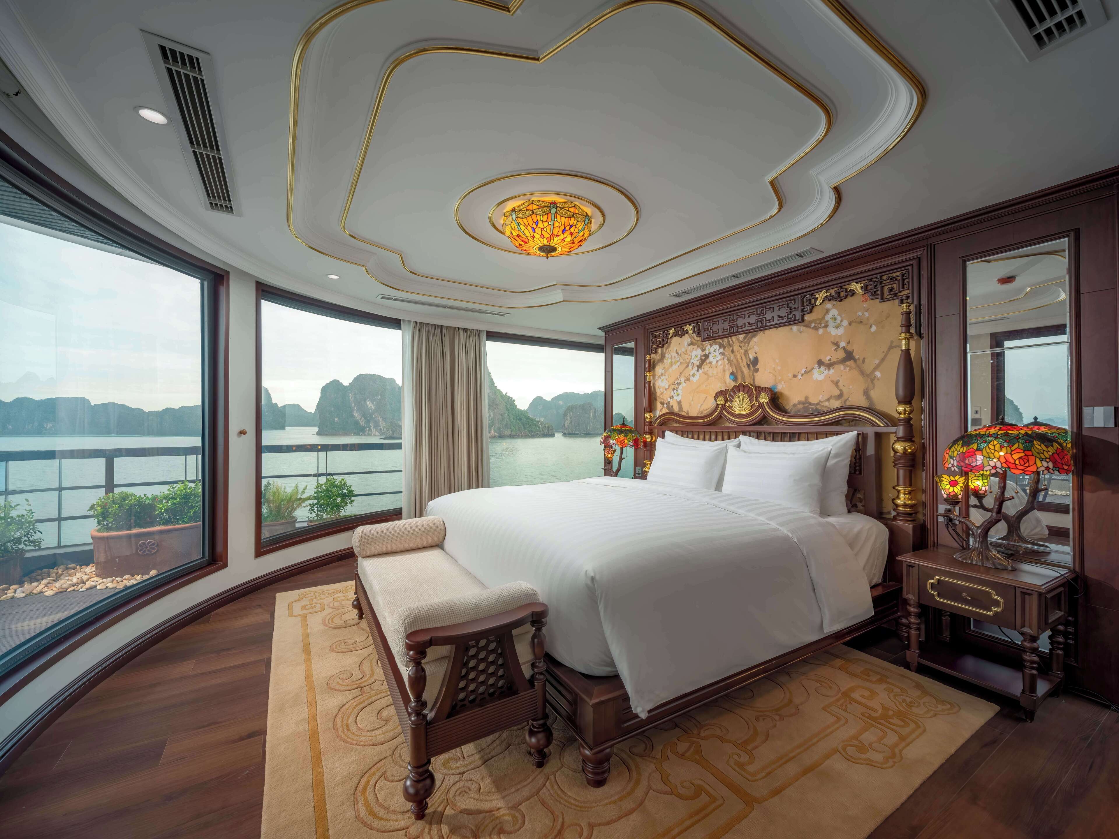 A spacious bedroom with a large bed, a bench, and a view of a lake.