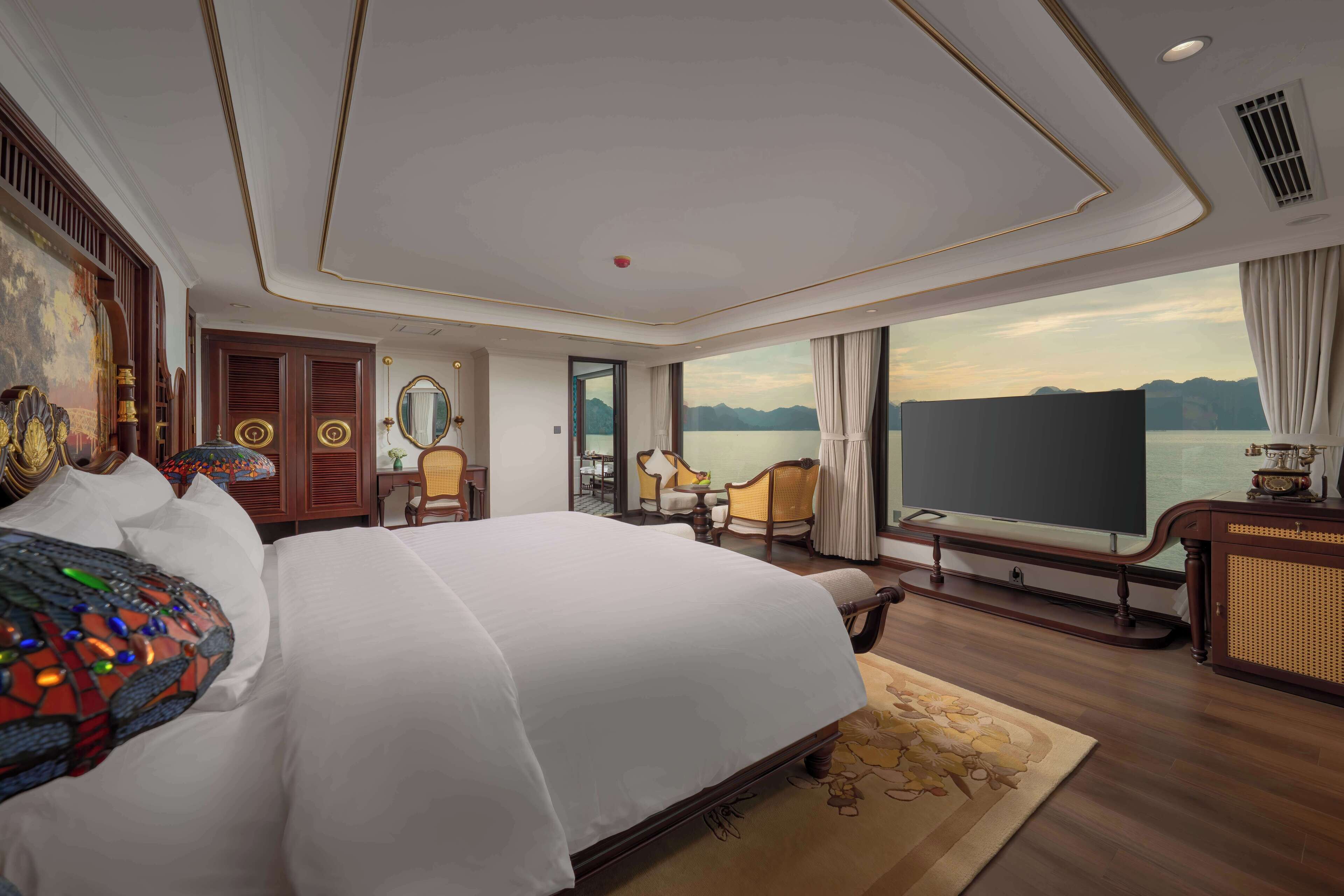 A spacious hotel room with a large bed, a television, a desk, and a view of a lake.