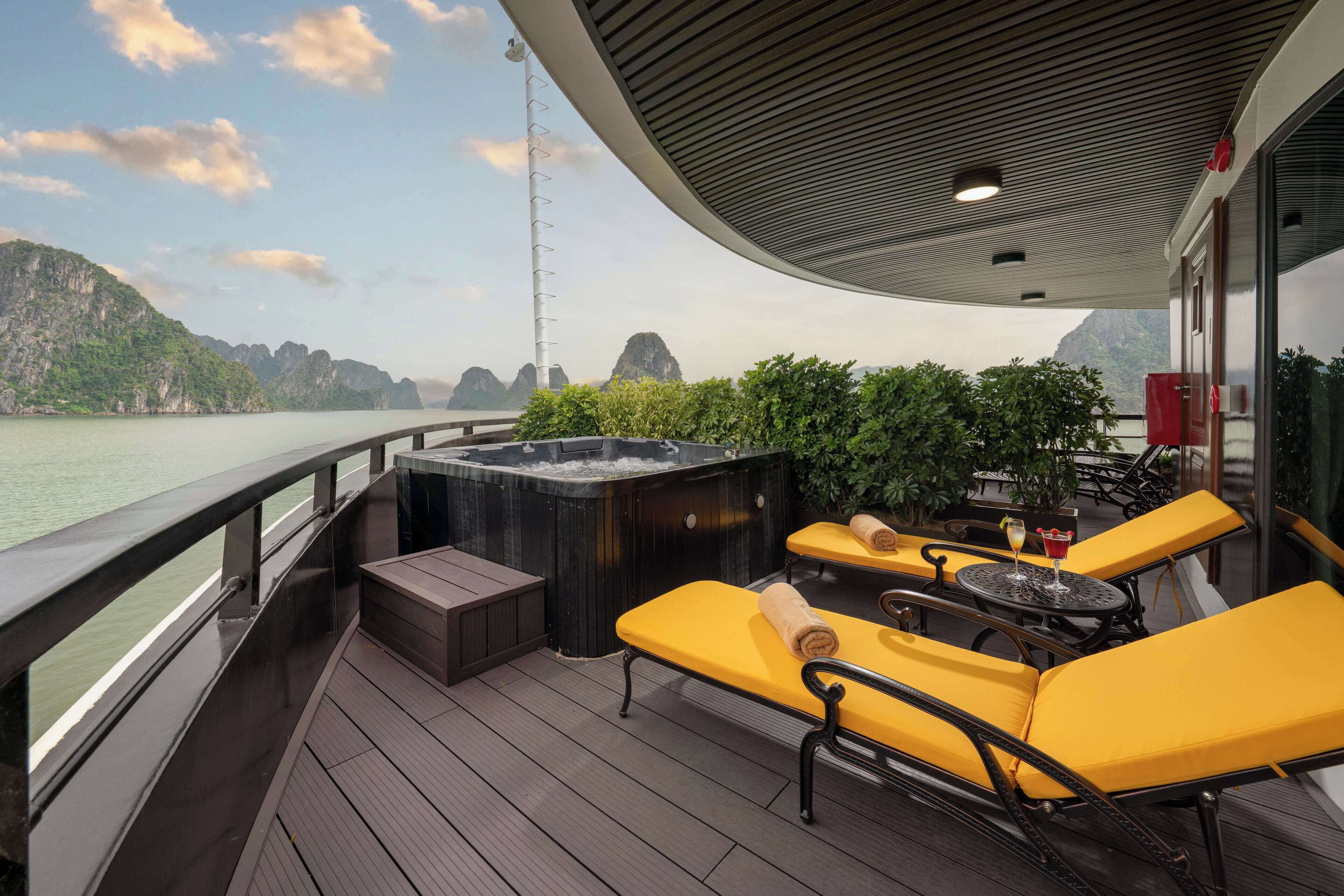 A deck with yellow lounge chairs, a hot tub, and a view of the water and mountains.