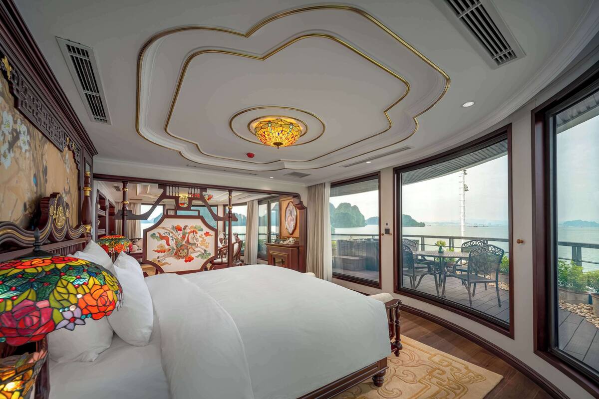 Une chambre spacieuse avec un grand lit, un plafond décoratif et un balcon offrant une vue sur l’eau.