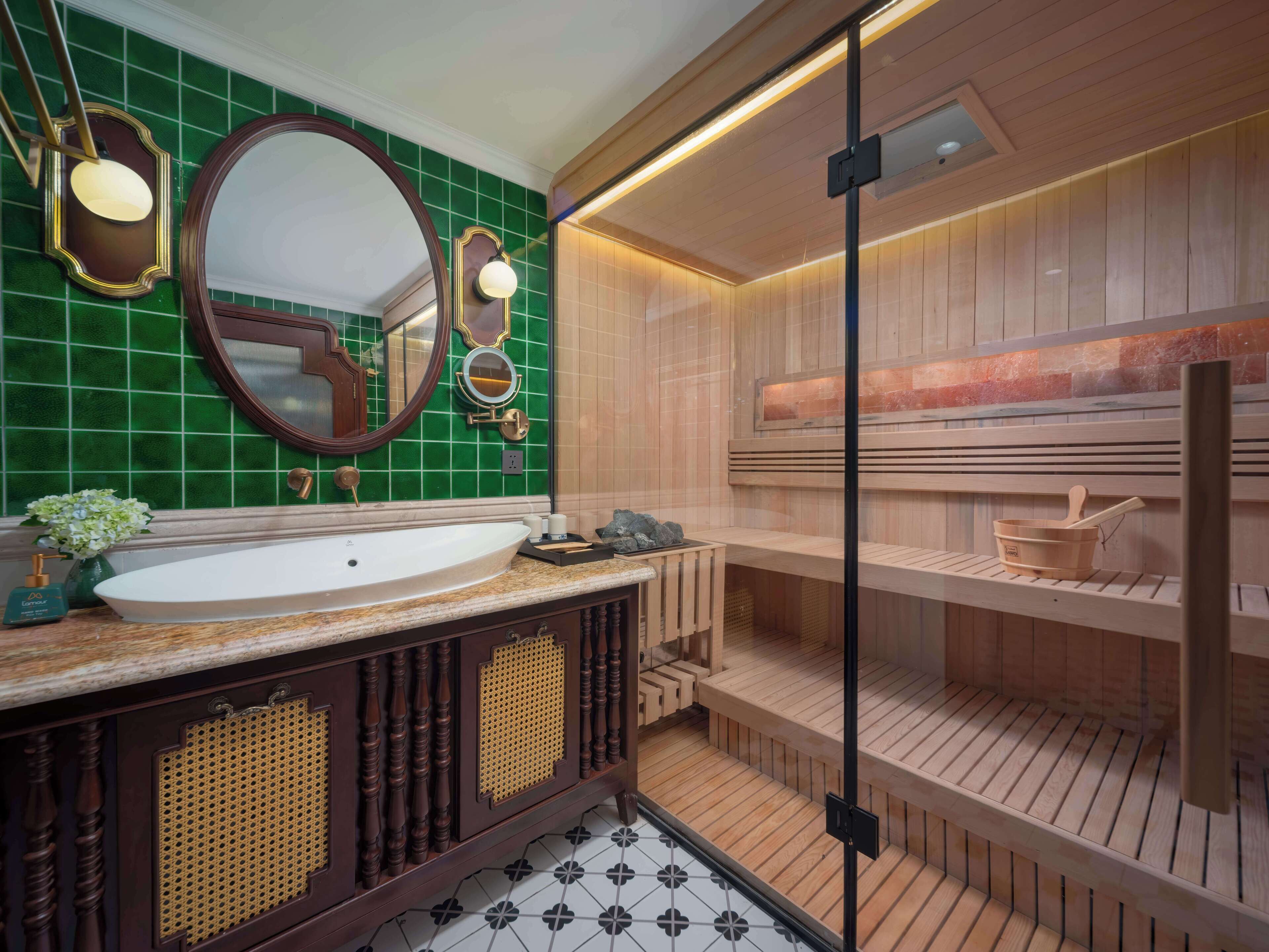 A bathroom with a large oval mirror, a white sink, and a wooden sauna area.
