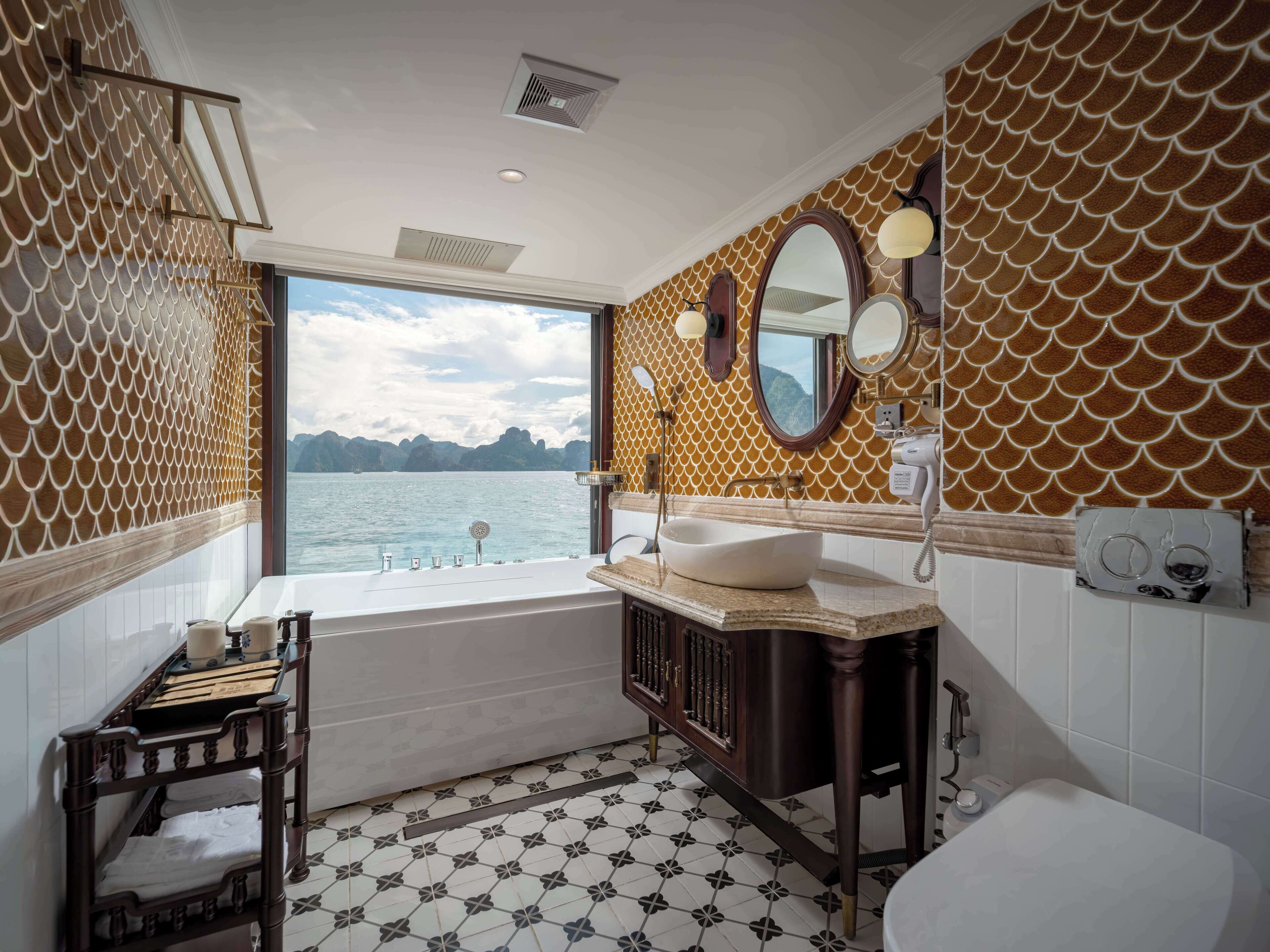 A bathroom with a bathtub, sink, and toilet, featuring a large window with a view of a body of water and mountains.