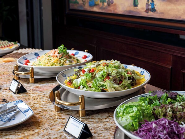 Una mesa de buffet con diversos platos, entre ellos ensaladas y un bol de ensalada de col.